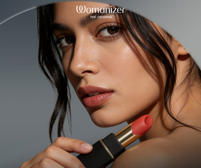 A close-up beauty ad showing a woman holding a lipstick tube. The lipstick bullet is a warm coral-red shade, and the case is black with a gold band.